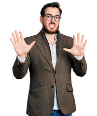 Young hispanic man wearing business jacket and glasses afraid and terrified with fear expression stop gesture with hands, shouting in shock. panic concept.