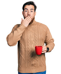 Young hispanic man holding coffee covering mouth with hand, shocked and afraid for mistake....