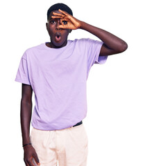 Young african american man wearing casual clothes doing ok gesture shocked with surprised face, eye looking through fingers. unbelieving expression.