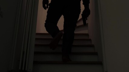 Mysterious man wearing black hoodie holding a pistol wearing a cloth mask covering his face completely in front of the door, Silhouette and dark concept image,threat of firearms,attack or defense.