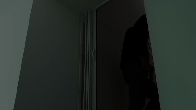 Mysterious man wearing black hoodie holding a pistol wearing a cloth mask covering his face completely in front of the door, Silhouette and dark concept image,threat of firearms,attack or defense.