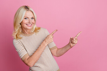 Photo of toothy beaming person with blond hair dressed striped t-shirt indicating at empty space sale isolated on pink color background