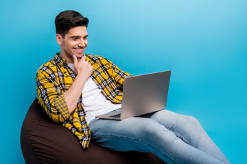 Photo of young glad programmer man touch chin decide which content is better for his blog using laptop isolated on blue color background