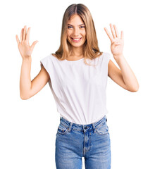 Beautiful caucasian woman with blonde hair wearing casual white tshirt showing and pointing up with fingers number nine while smiling confident and happy.