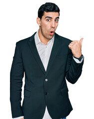 Handsome hispanic man wearing business clothes surprised pointing with hand finger to the side, open mouth amazed expression.