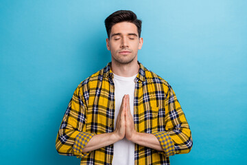 Photo of dreamy attractive guy wear yellow checkered shirt closed eyes arms together praying isolated blue color background