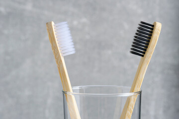 Two wooden toothbrushes with black and white bristles in a glass in bathroom.