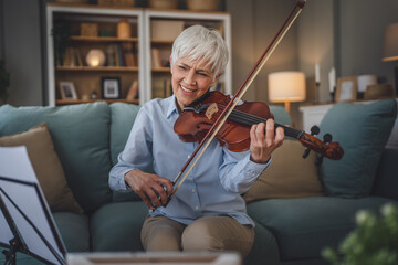 Mature senior caucasian woman learn to play violin practice at home