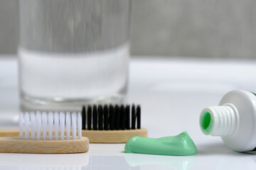 Glass water, two wooden toothbrushes and green coniferous toothpaste in bathroom.