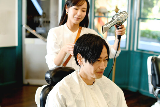 男性客の髪をドライヤーで乾かすアジア人の女性美容師