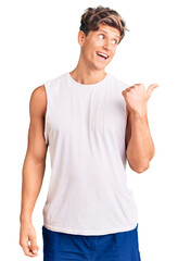 Young handsome man wearing sleveeless t shirt smiling with happy face looking and pointing to the side with thumb up.