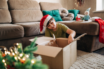 Kid boy decorating Christmas tree put off balls from the box authentic real celebration image...