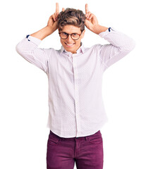 Young handsome man wearing business clothes and glasses posing funny and crazy with fingers on head as bunny ears, smiling cheerful