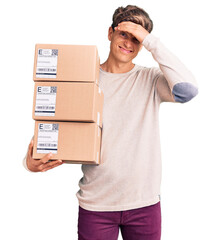 Young handsome man holding delivery package stressed and frustrated with hand on head, surprised...