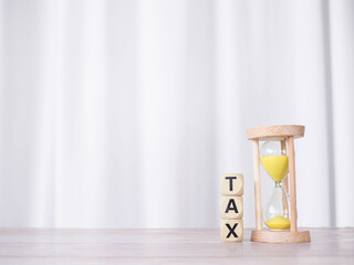 Hourglass and wooden blocks with the word TAX on stack of coins. The concept for manage time to...
