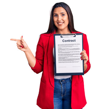 Young beautiful brunette woman holding clipboard with contract smiling happy pointing with hand and finger to the side