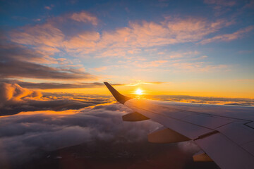 Airplane flight in sunset sky over ocean water and wing of plane. View from the window of the...