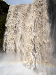 Detail of a powerful waterfall in Iceland. Muddy coloured water. Faint rainbow at the bottom of the falls.