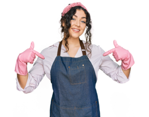 Young hispanic girl wearing cleaner apron and gloves looking confident with smile on face, pointing oneself with fingers proud and happy.