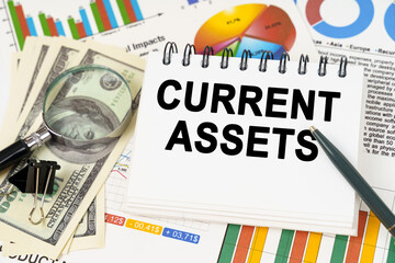 On the table are business charts, dollars and a notepad with the inscription - CURRENT ASSETS