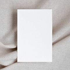 Empty paper card mockup on blurred folded neutral beige linen textile with soft natural shadows,...