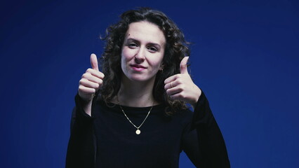 Positive Young Woman Giving Thumbs Up, Blue Background Signifying Approval