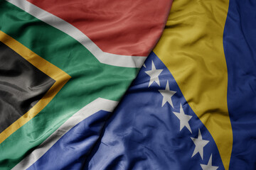big waving national colorful flag of bosnia and herzegovina and national flag of south africa .