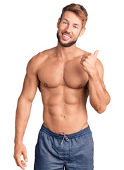 Fototapeta premium Young caucasian man standing shirtless smiling with happy face looking and pointing to the side with thumb up.