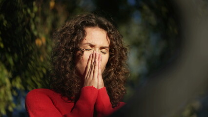 Stressed woman feeling regret by covering face in preoccupation standing outside with sun shining...