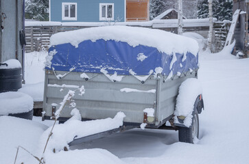 A trailer for a car covered with an awning in the snow. Transportation of belongings.