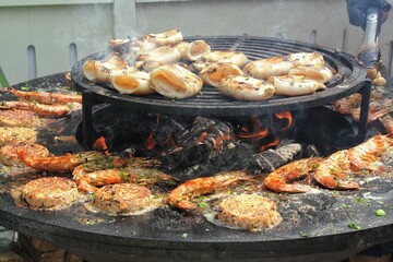 Seafood slices are cooked on a fire pit surface in the shape of cone shaped bowl. Bowl-shaped flat grill with squid and prawn. Outdoor barbecue cooking. Street food concept. Toast the hot grilled