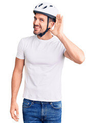 Young handsome man wearing bike helmet smiling with hand over ear listening an hearing to rumor or gossip. deafness concept.