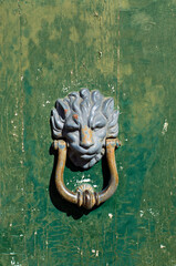 Detailed view vintage metal door knocker in the form of a lion's head on an old green chipped paint wooden door.