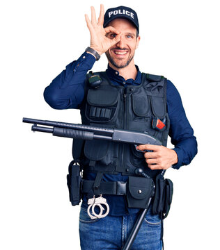 Young handsome man wearing police uniform holding shotgun doing ok sign with fingers, smiling friendly gesturing excellent symbol