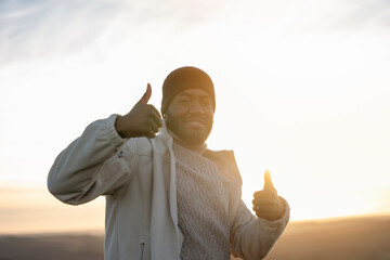 Man giving thumb up to at sunset nature background. Enjoy hiking and exploring new places concept toned image