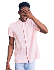 Young african american man wearing casual clothes peeking in shock covering face and eyes with hand, looking through fingers with embarrassed expression.