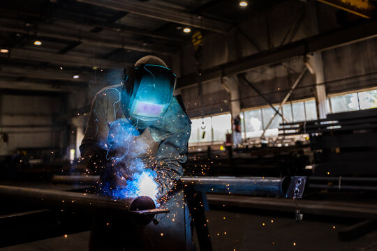 The welder works in the workshop. The moment of welding of metal structures. Beautiful sparks during welding of various metal elements in the workshop. The welder is working hard.