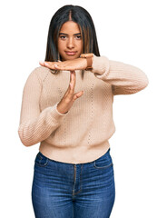 Young latin girl wearing wool winter sweater doing time out gesture with hands, frustrated and...