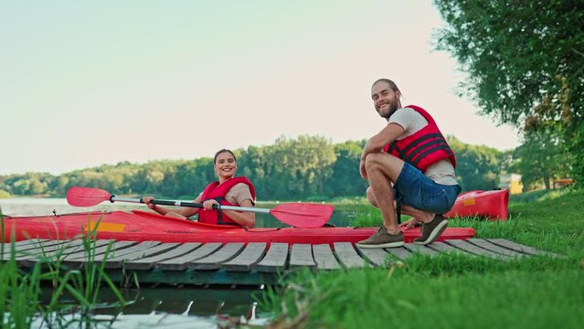 Beautiful Caucasian woman wearing red vest and talking with her man while sitting in kayak. Happy female enjoying canoe at summer day. People resting on lake or pond. Recreation concept.