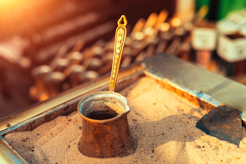 Traditional delicious Turkish dibek coffee being prepared in a copper coffee pot on stove filled with hot sand. 