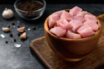 Diced raw chicken breast in wooden bowl on black background.