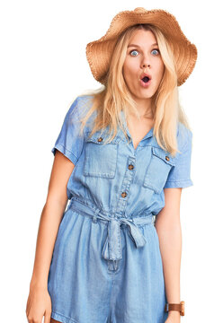 Young beautiful blonde woman wearing summer hat and dress afraid and shocked with surprise expression, fear and excited face.