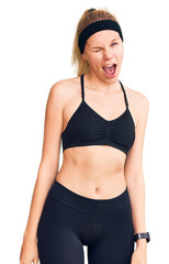 Young beautiful blonde woman wearing sportswear winking looking at the camera with sexy expression,...