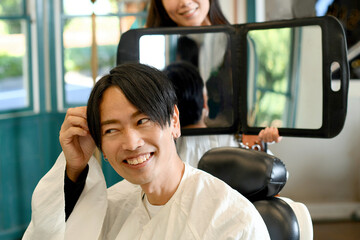 男性客に鏡を見せる美容師のアジア人女性