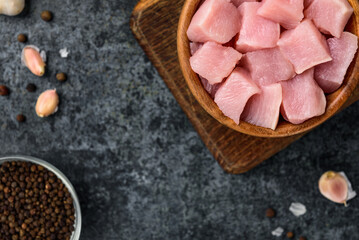 Diced raw chicken breast in wooden bowl on black background.