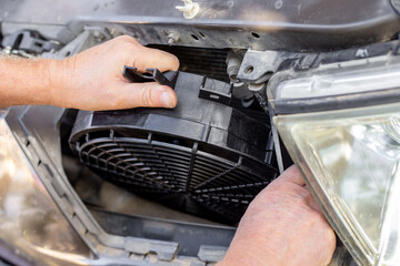 A car mechanic installs a car engine cooling fan under the radiator grille. Auto repair and maintenance