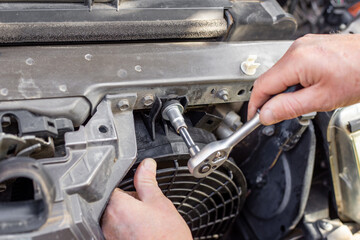 A man fixes an engine cooling fan under the radiator grill of a car. Machine maintenance and repair