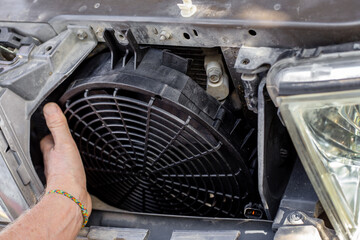 A man fixes an engine cooling fan under the radiator grill of a car. Machine maintenance and repair