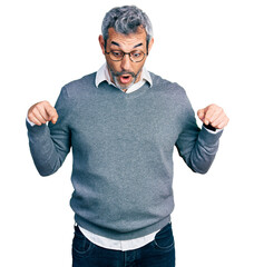 Middle age hispanic with grey hair wearing glasses pointing down with fingers showing...