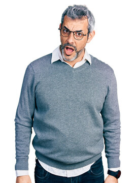 Middle age hispanic with grey hair wearing glasses in shock face, looking skeptical and sarcastic, surprised with open mouth